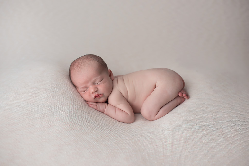 beautiful newborn baby boy on cream background in tushie up pose